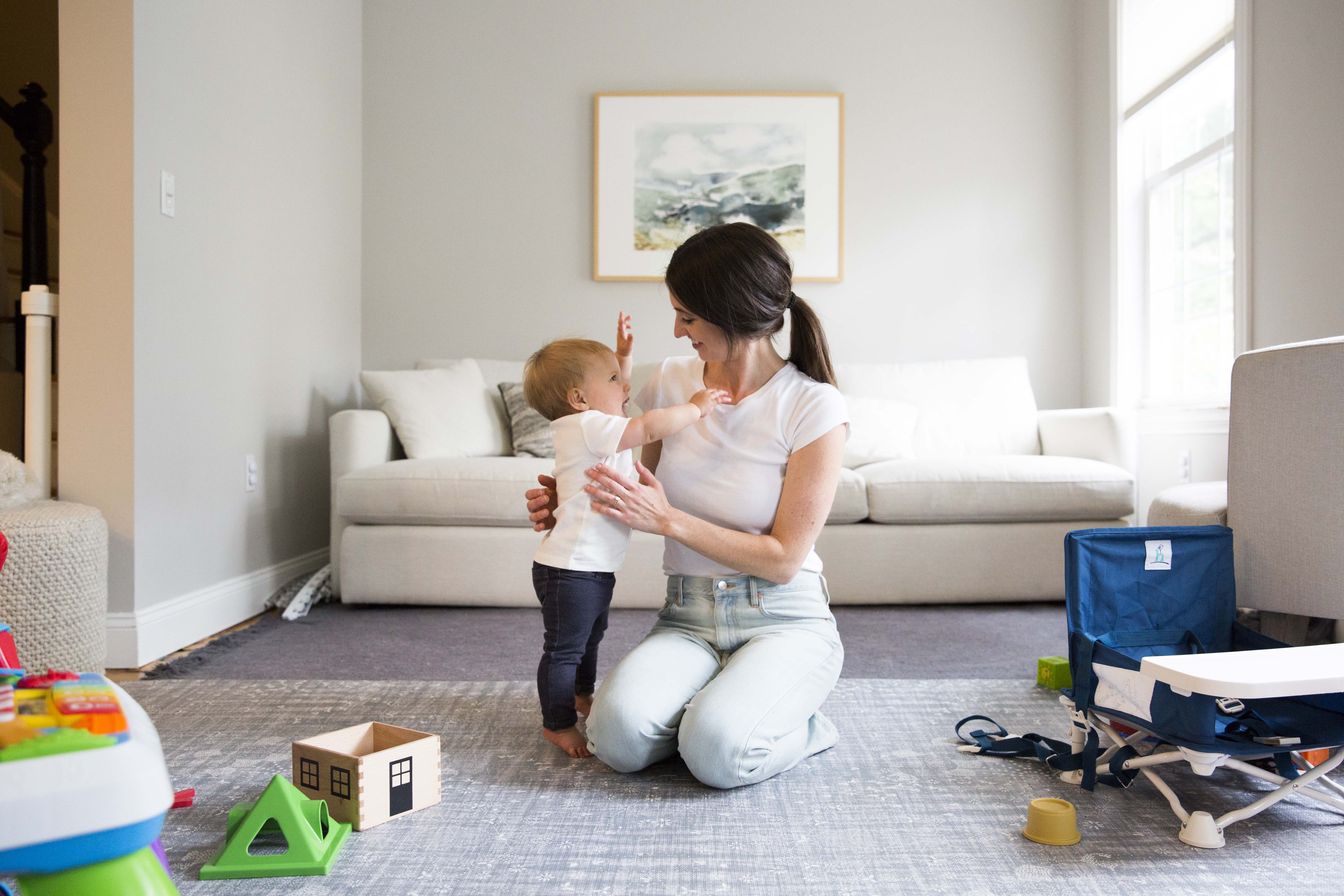 Jess Galica kneeling on a carpet with a baby on her left and a white couch behind