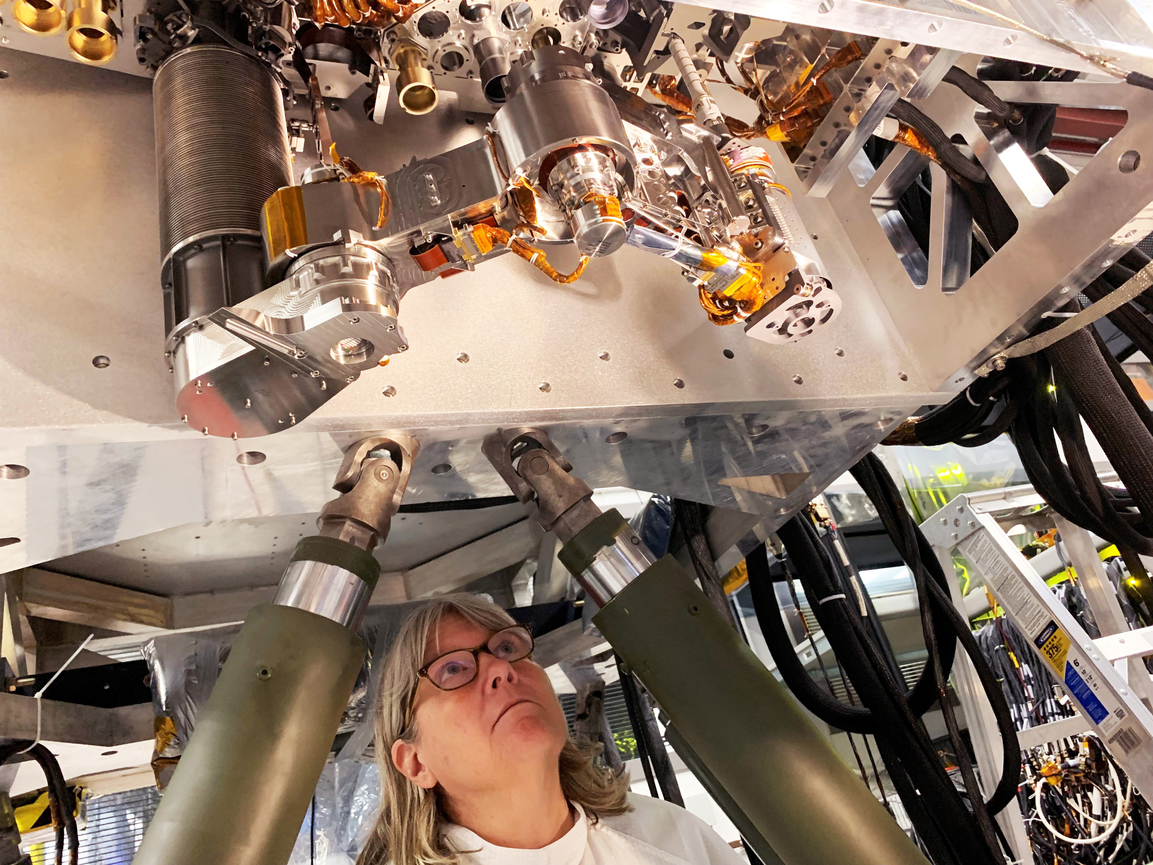 A photo of MIT alum Louise Jandura standing underneath a piece of machinery/equipment