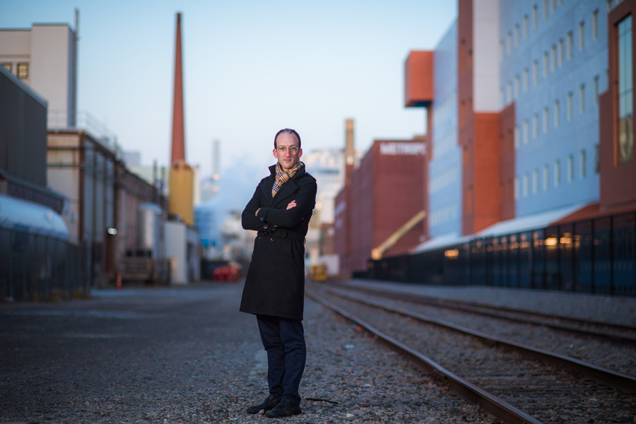 Man in jacket standing near train tracks with city skyline 