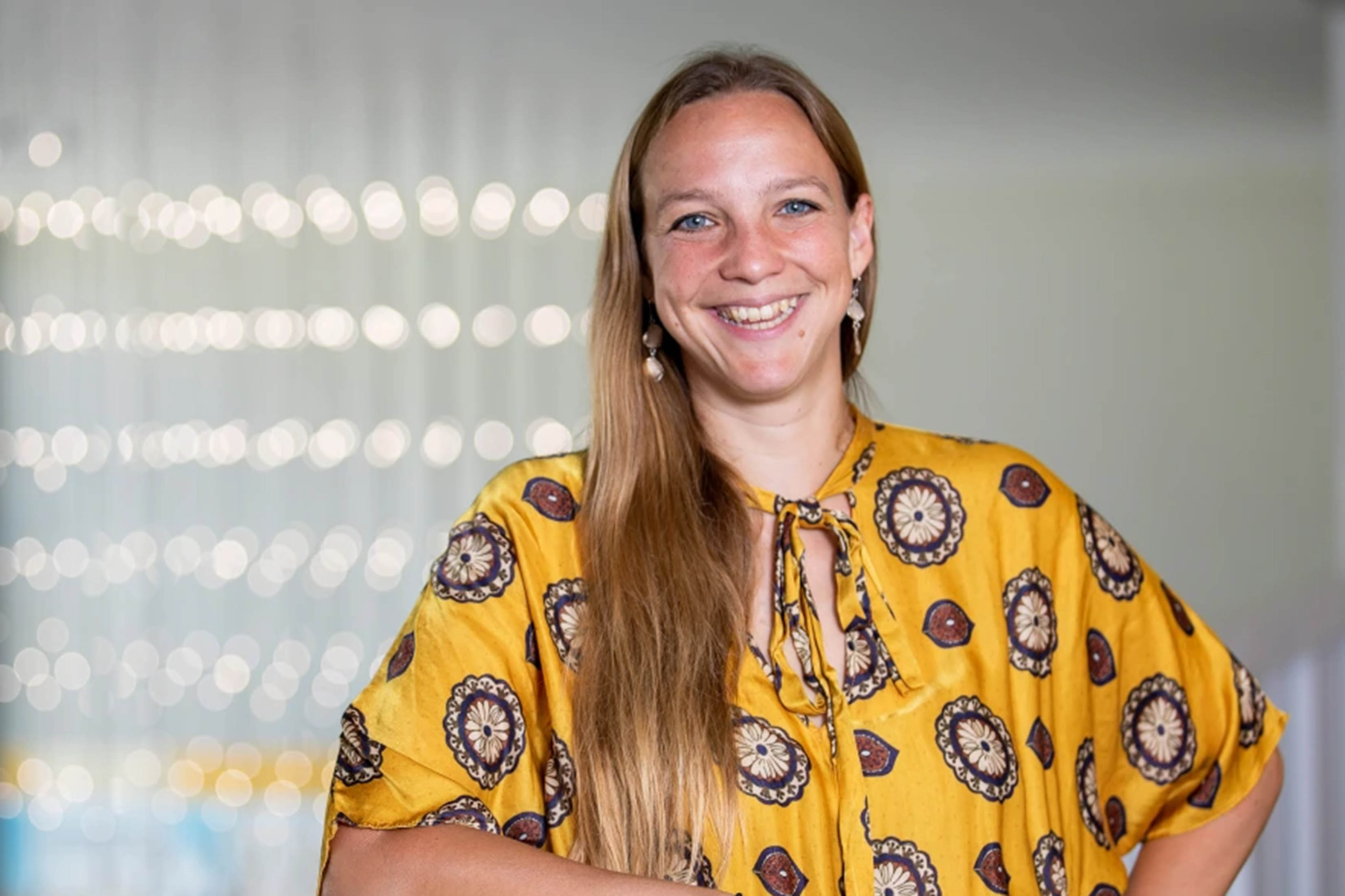 Head and shoulders portrait of Mariel Borowitz ’06 wearing a patterned yellow shirt in front of a white background dotted with lights