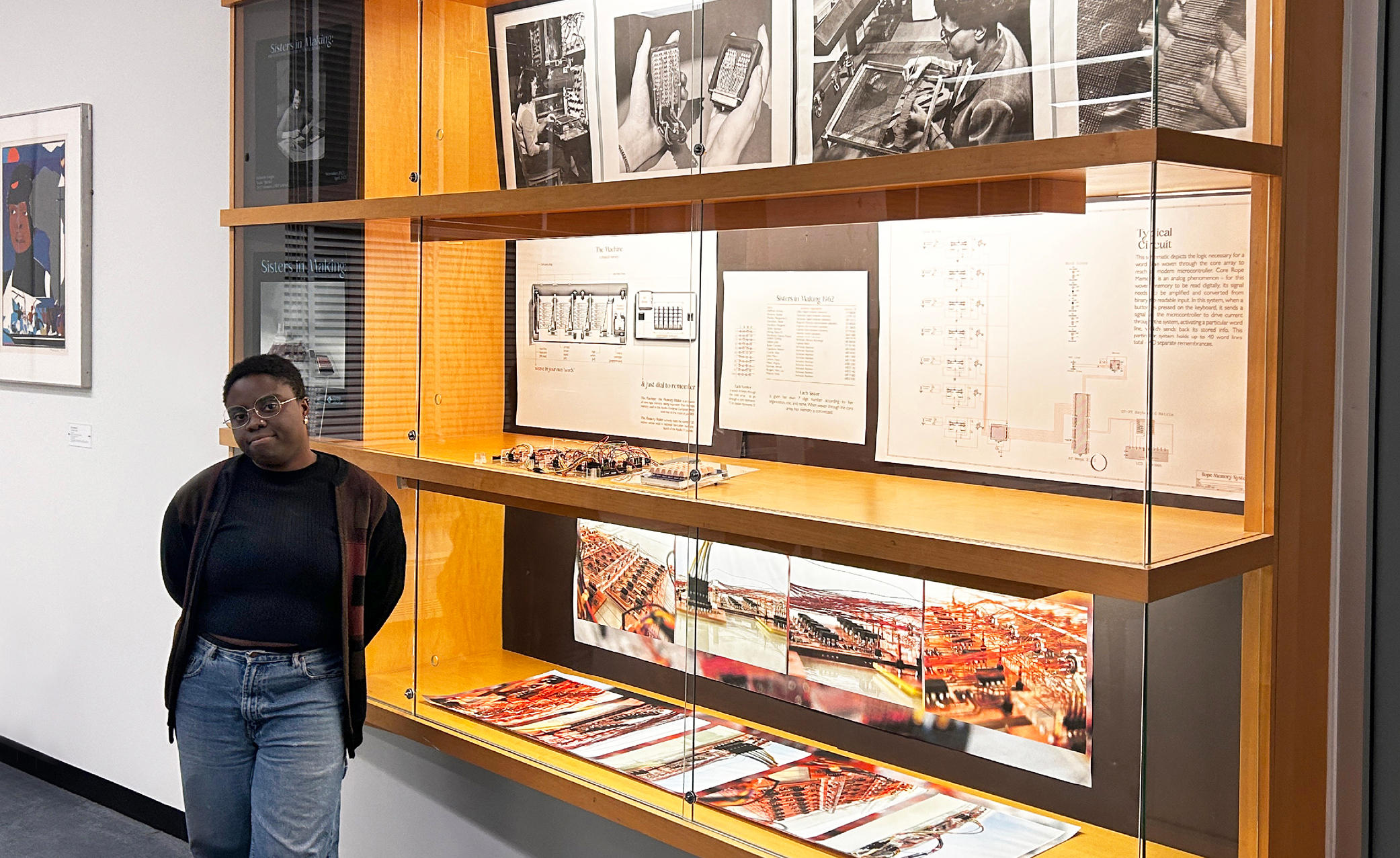 Deborah Tsogbe stands to the left of a large display case in the MIT Rotch Library