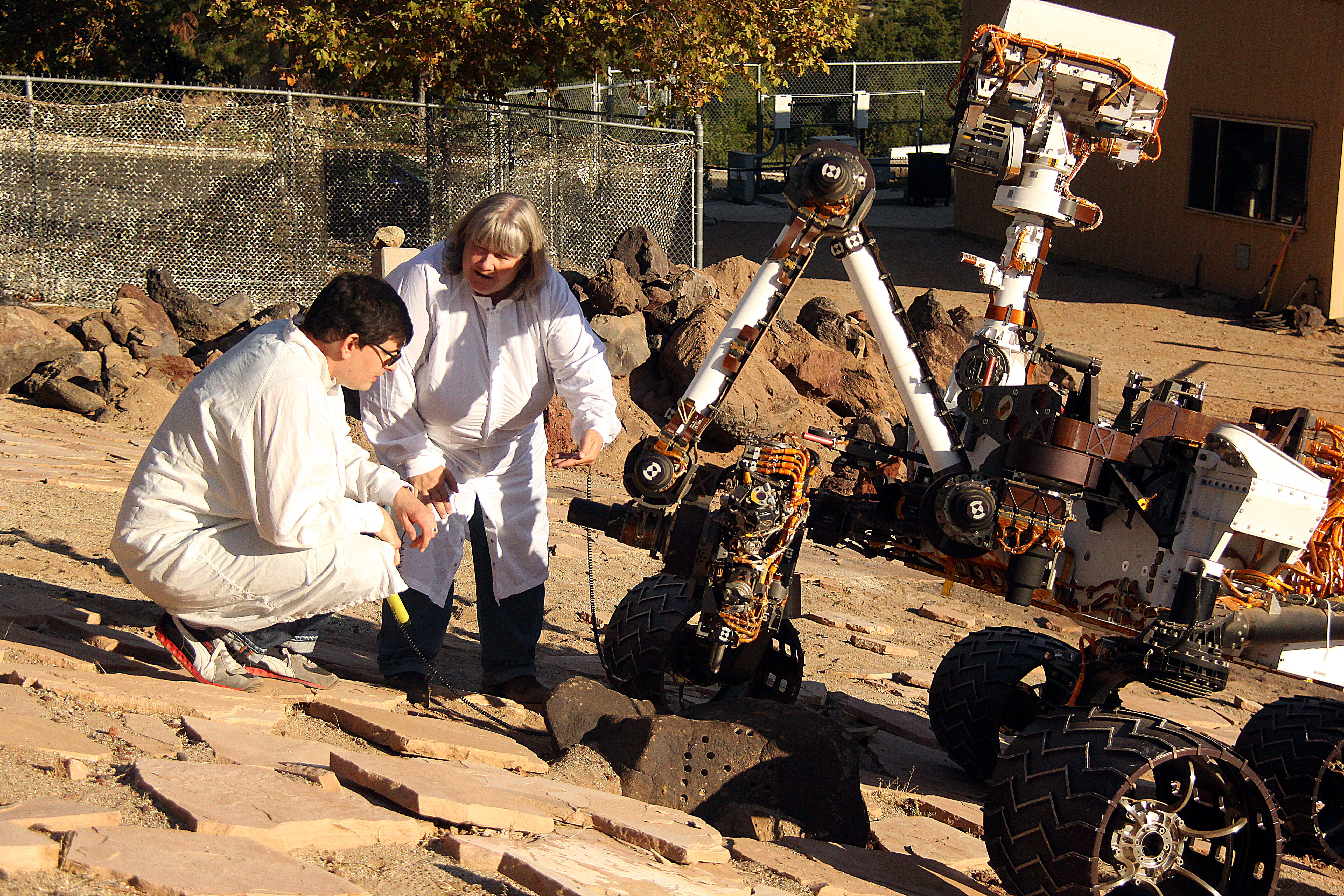 MIT alum Louise Jandura in an all white suit talking to a colleague on a rocky service with a rover/machine