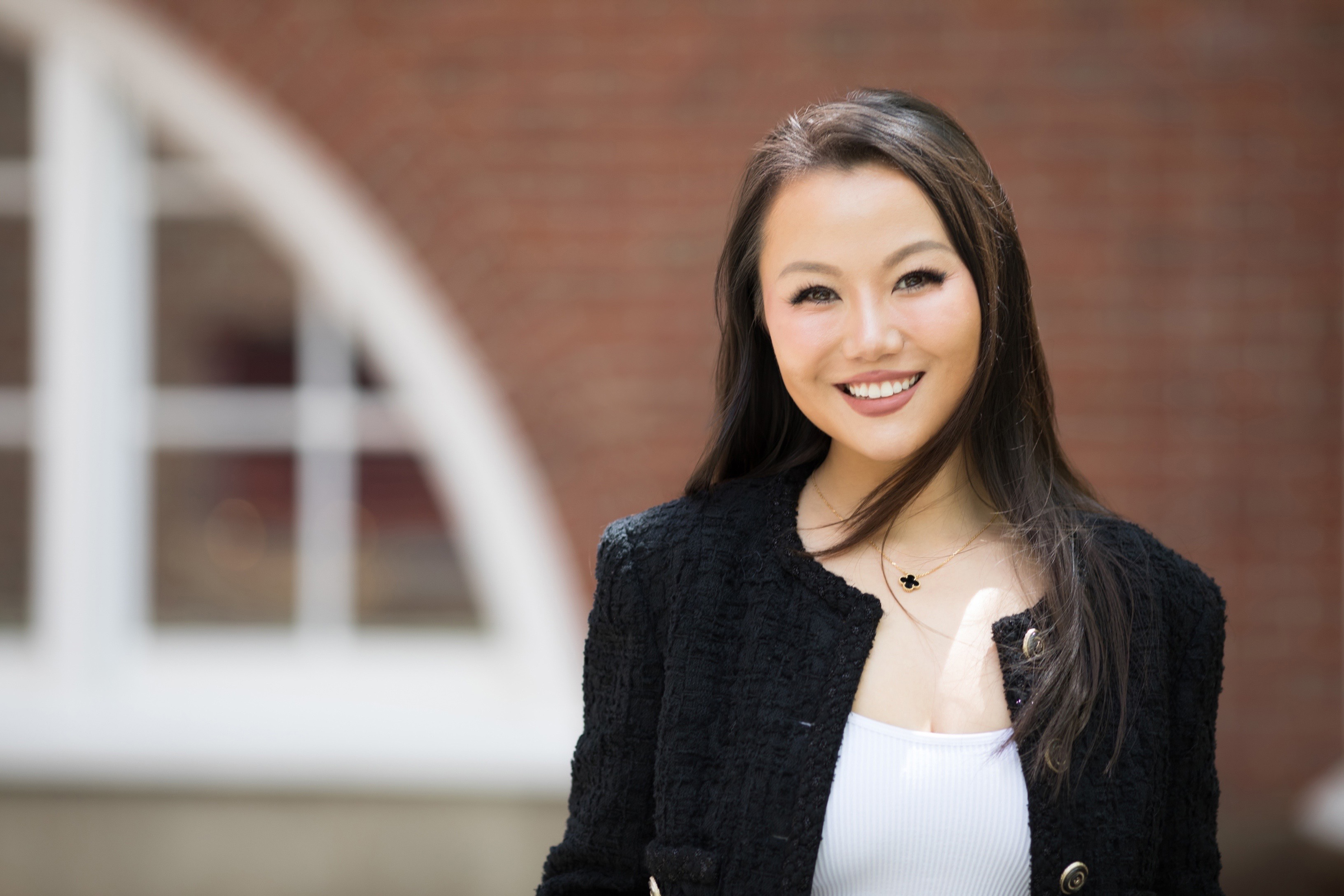 A photo of Sophie Bai standing outside with a brick wall behind her with a large cutout semi-circular window