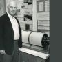 A black and white photo of MIT alum Lynn Sykes standing next to a spherical piece of equipment